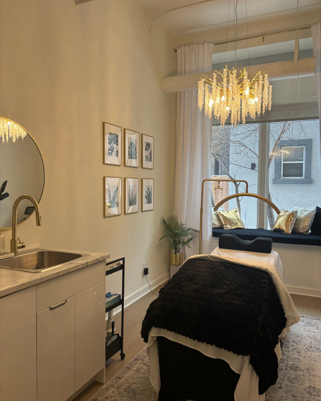A modern beauty suite with a sink, framed wall art and a treatment bed near a window