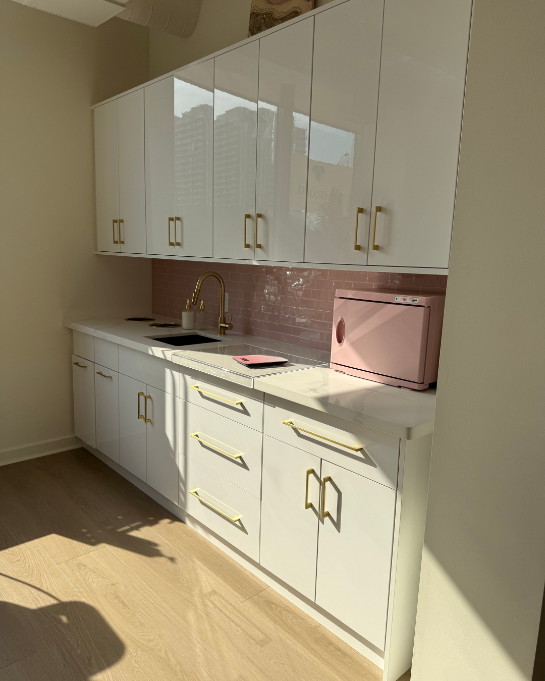 A modern salon suite with white cabinetry, gold hardware and a pink countertop